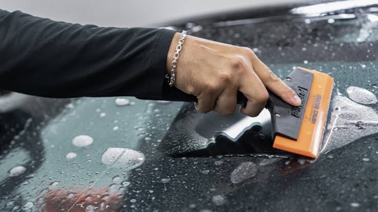 Installer squeegeeing protective film across automotive glass with a felt-edged squeegee