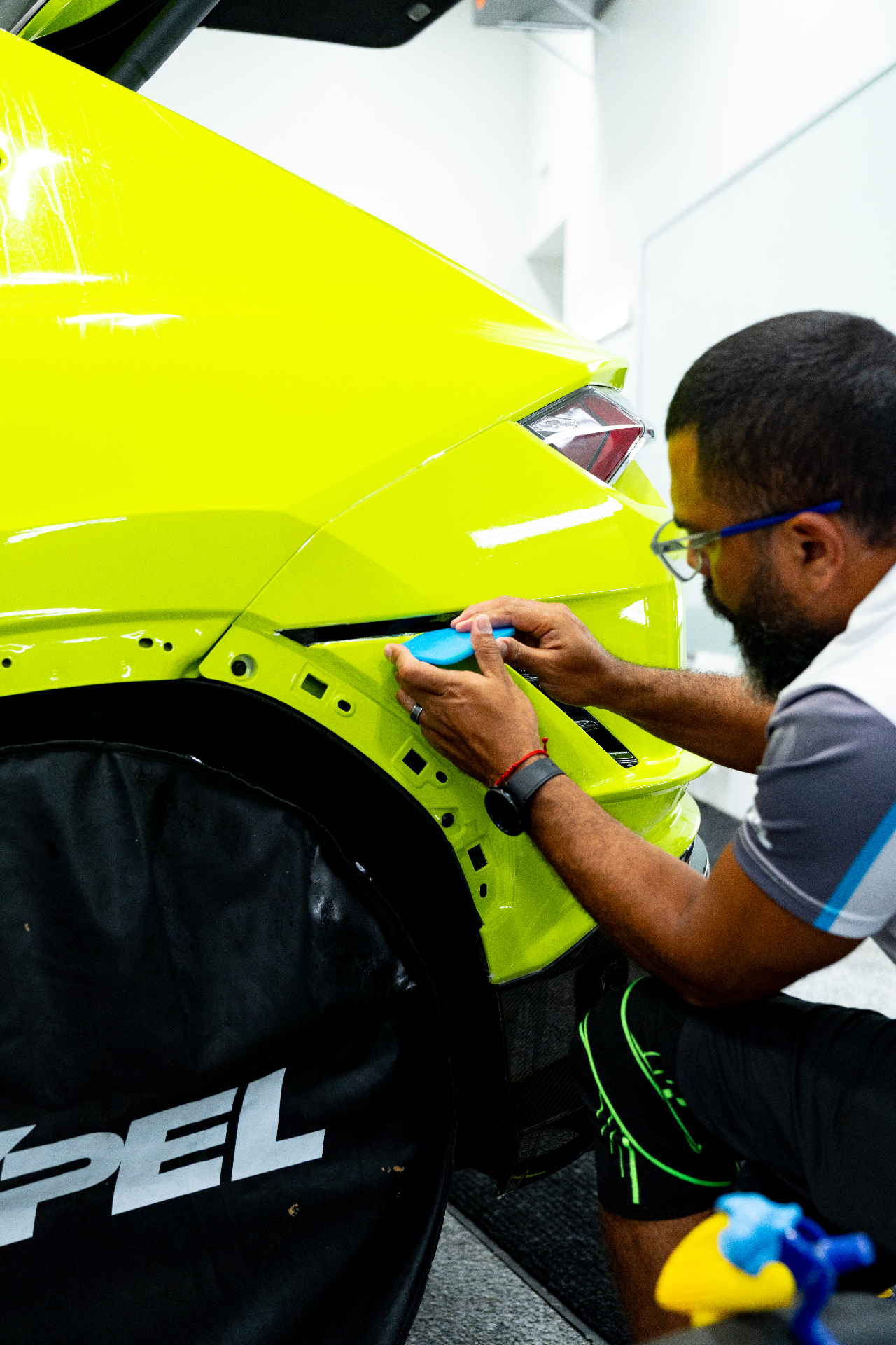 XPEL certified installer applying paint protection film to an acid yellow sports car rear quarter panel