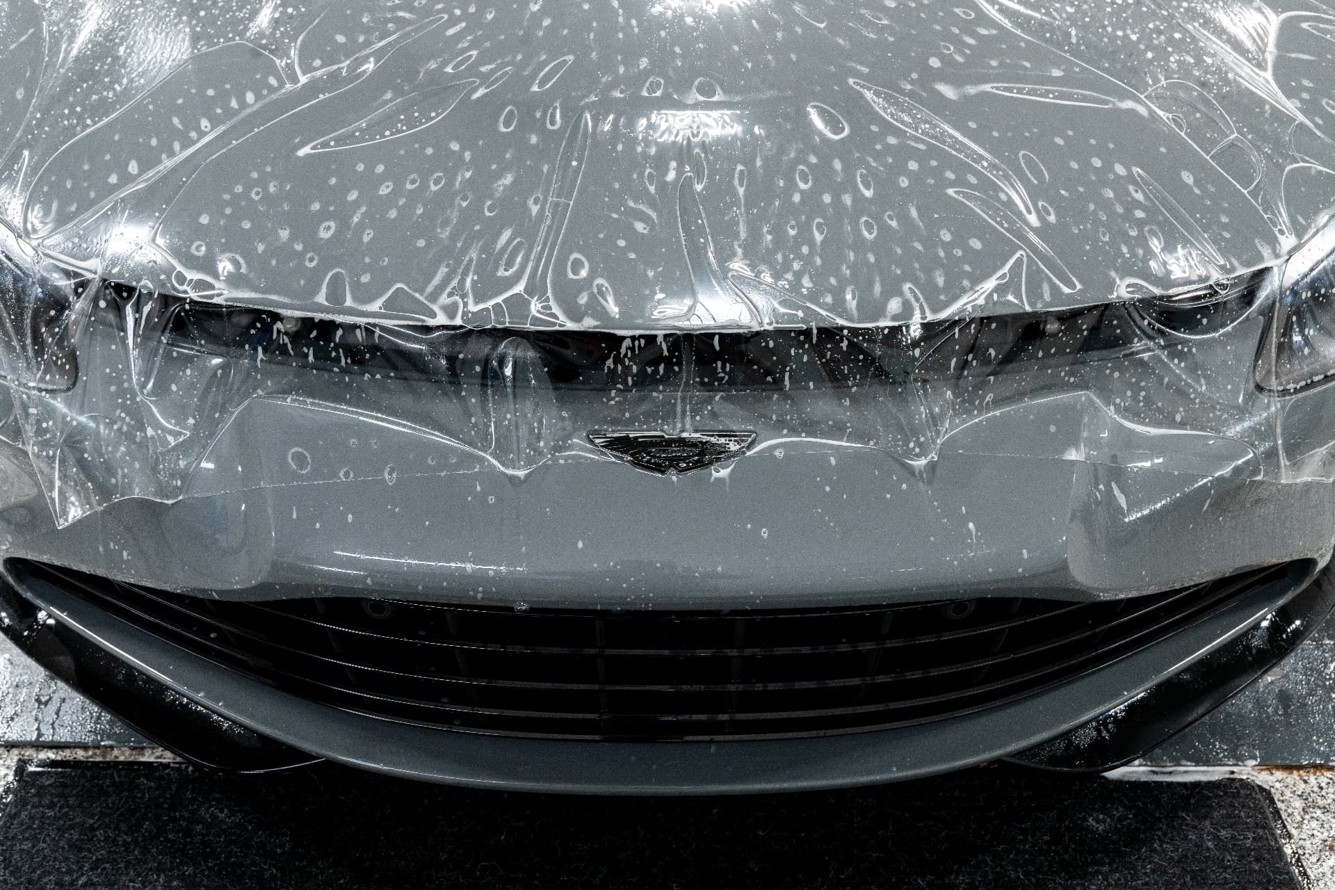 Paint protection film being applied to the front end of a grey Aston Martin