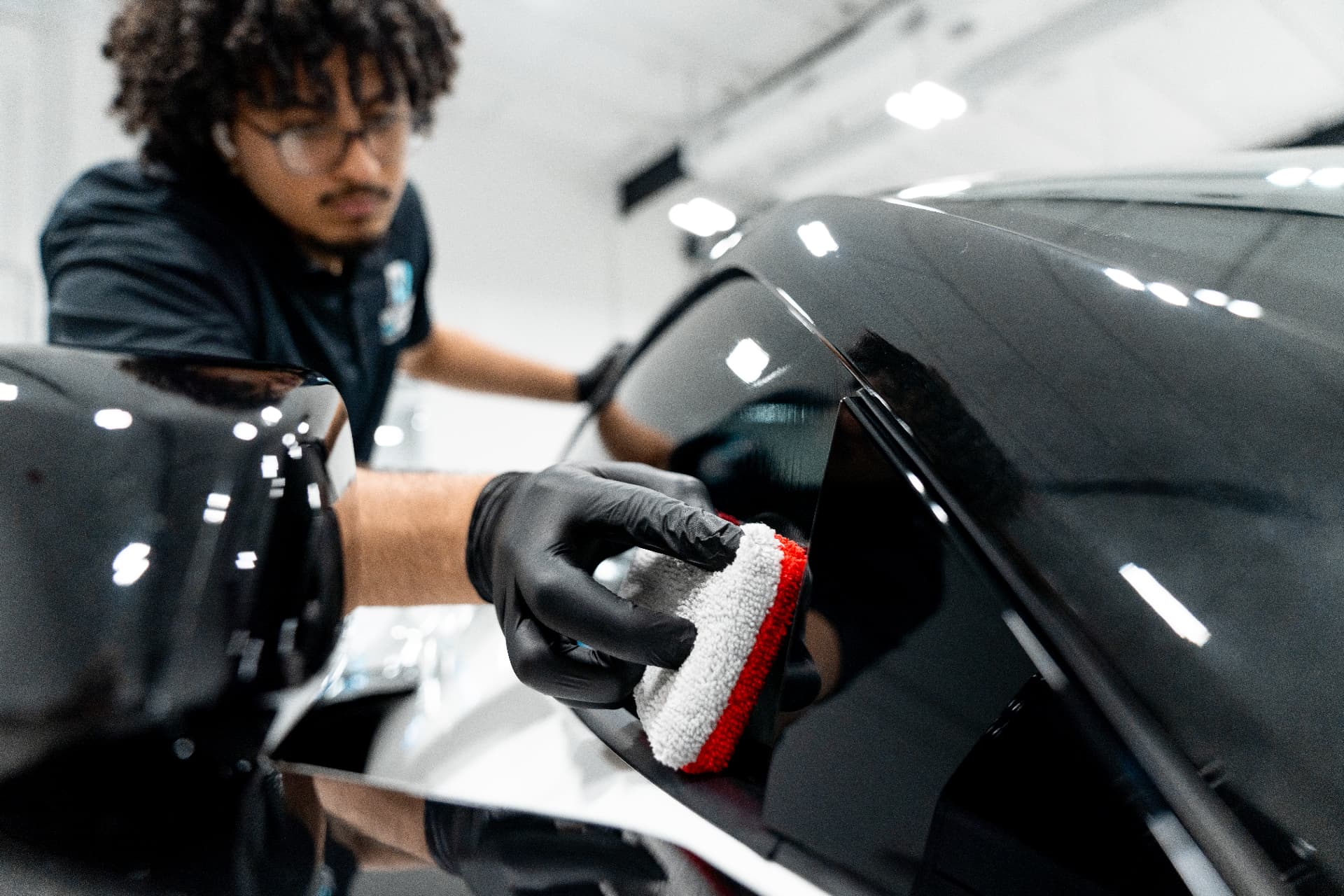 Gloved technician applying XPEL ceramic coating with an applicator pad on a dark vehicle