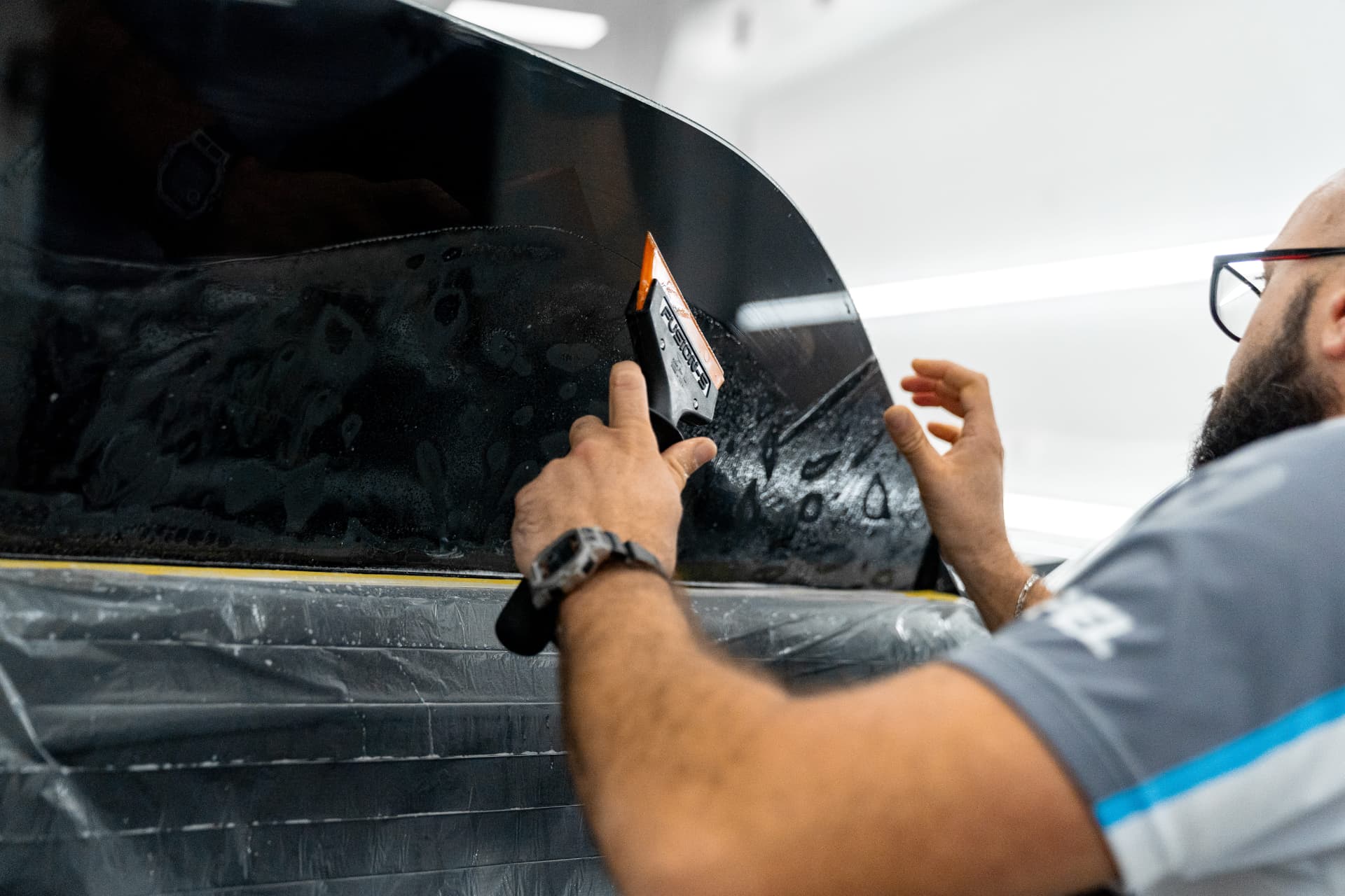 XPEL installer squeegeeing ceramic window tint film onto a car side window in the Naples studio